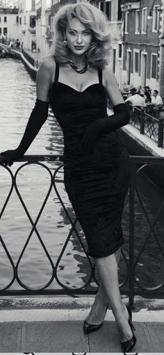 Woman in a black dress and long gloves posing by a canal