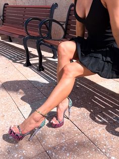 Woman in a black dress and snakeskin print high heels sitting on a bench