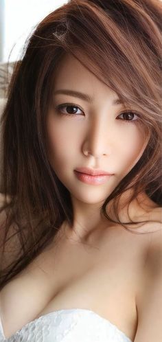 Woman with long brown hair wearing a white top, looking directly at the camera