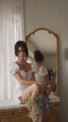 Woman in a white dress and pearl necklace sitting indoors with a mirror reflection