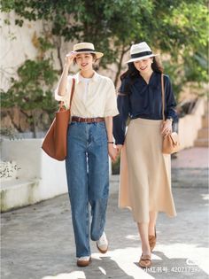 Two women in hats and casual outfits holding hands outdoors
