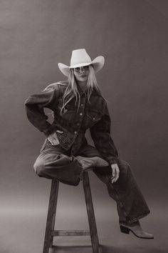 Woman in a cowboy hat and denim outfit sitting on a stool in a studio