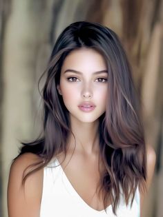 Woman with long brown hair wearing a white top, looking directly at the viewer