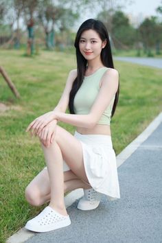 Woman with long black hair wearing a crop top and white skirt, squatting outdoors