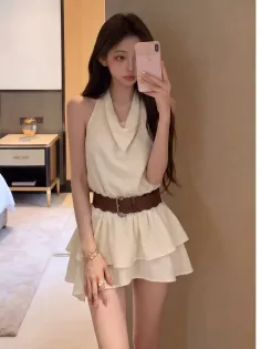 Woman in a light-colored halter top and mini skirt with a brown belt indoors