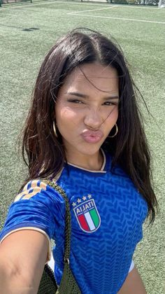 Woman in a blue soccer jersey making a kissy face on a soccer field