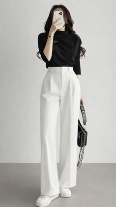 Woman in a black top and white pants holding a phone to her face