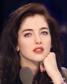 Woman with long dark hair and blue eyes, wearing red lipstick, with a microphone
