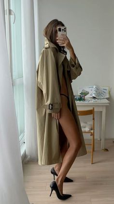 Woman in a trench coat and black heels taking a mirror selfie