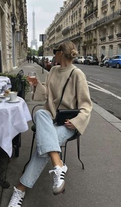 Woman with a hair bun and sunglasses sitting at an outdoor cafe with the Eiffel Tower in the background