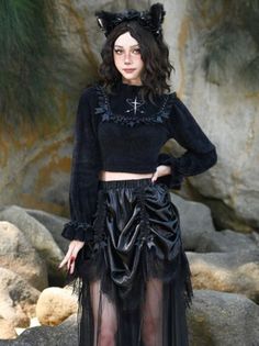 Woman in a black gothic outfit with cat ears posing against a rocky background