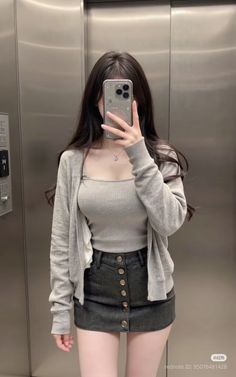 Woman in a gray crop top and denim skirt taking a mirror selfie in an elevator