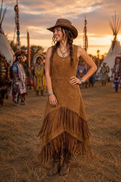 Woman in a cowboy hat and fringe dress at sunset with tipis in the background