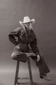 Woman in a cowboy hat and denim outfit sitting on a stool in a studio