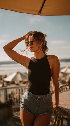 Woman in denim shorts and a black top on a beach at golden hour