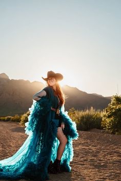 Woman in a cowboy hat and teal dress with fishnet stockings at sunset