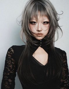 Woman with long gray hair and dark makeup wearing a black top with lace sleeves