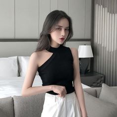 Woman with long dark hair wearing a black top and white pants indoors