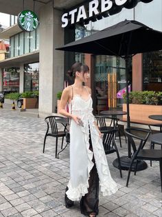 Woman in a white ruffled dress and black sheer pants standing outdoors