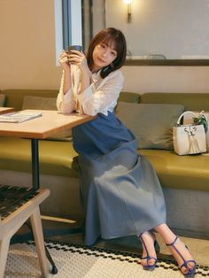 Woman in a white blouse and blue skirt sitting in a cafe with a mug