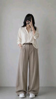 Person in a white shirt and wide leg pants taking a mirror selfie