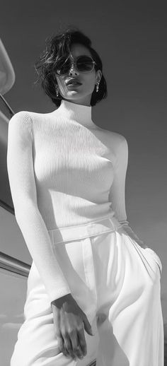 Woman with short hair and sunglasses wearing a white turtleneck and pants