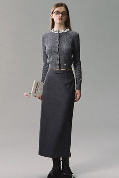 Woman in a gray cardigan and long skirt holding a book with a flower