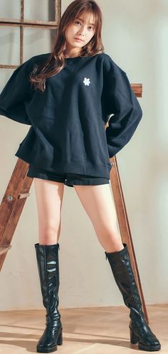 Woman in a black sweatshirt, black shorts, and black boots standing indoors