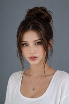 Woman with brown hair in a bun and a cross necklace against a gray background