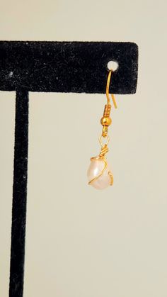 A single gold wire-wrapped earring with a pink pearl on a black display stand