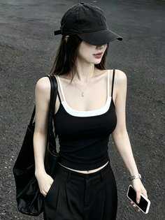 Woman in a black tank top and cap holding a phone outdoors