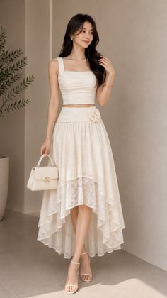 Woman in a white lace crop top and high-low skirt holding a white handbag