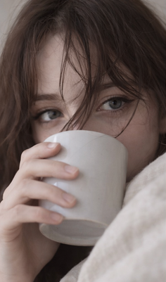 Close up of a person with brown hair and blue eyes drinking from a mug