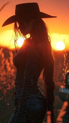 Woman in a cowboy hat with long hair silhouetted against a golden hour sunset