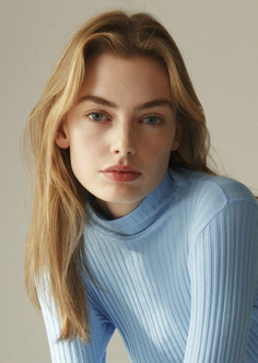 Woman with blonde hair and blue eyes wearing a light blue turtleneck
