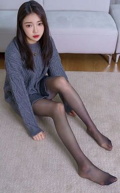 Woman in a gray sweater and black tights sitting on a carpet indoors