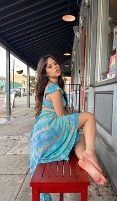 Woman with long hair in a tie-dye dress sitting on a red bench outdoors