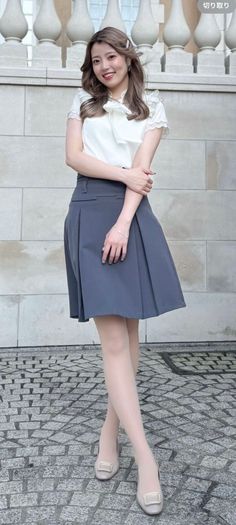 Woman in a white blouse and pleated skirt posing outdoors