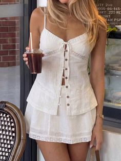 Woman in a white two-piece outfit holding a drink outdoors