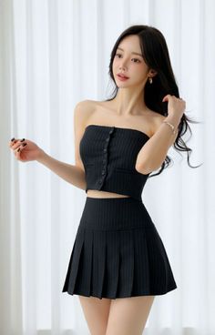 Woman with long black hair wearing a strapless top and pleated mini skirt indoors