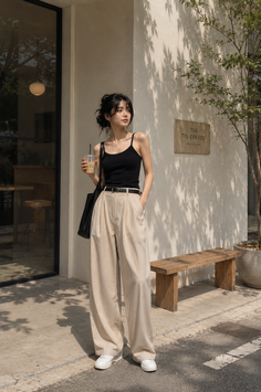 Woman in a black tank top and wide leg pants holding a drink outside a coffee shop