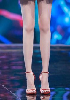 Person in red high heels with black nail polish standing on a stage