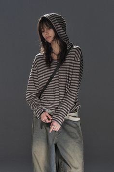 Person in a striped hoodie and baggy jeans looking down against a dark background