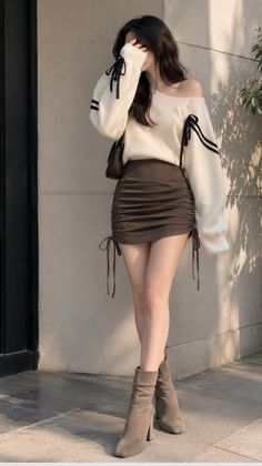 Woman in an off-shoulder sweater and mini skirt with high heel boots outdoors