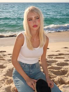 Woman with blonde hair in a white tank top and blue jeans on a beach