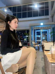 Woman with long black hair wearing a black top and white skirt indoors at night