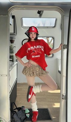 Woman in a red t-shirt and plaid skirt posing inside a camper van