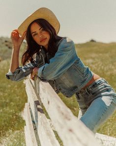 Woman in a cowboy hat and denim jacket leaning on a fence in a field