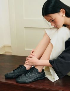 Woman with long black hair wearing black sneakers and a white dress, sitting indoors