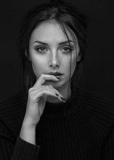 Woman with dark hair in a black sweater, hand near her mouth, in black and white